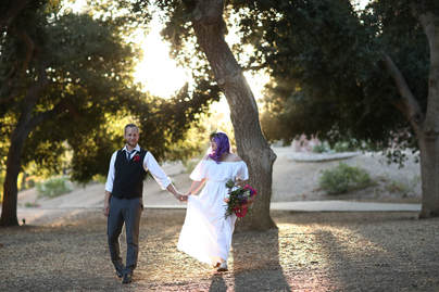 Groom and Bride with purple hair walking through the oak trees at this intimate wedding.