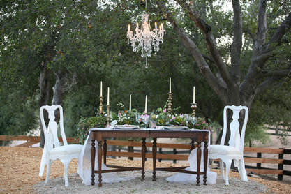 Small wedding table under a chandelier hung in the oak trees at a private venue.